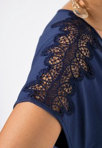 Top azul marino con intrincados detalles de encaje en las mangas, fabricado con un tejido suave y de textura agradable, y un diseño de corte relajado.