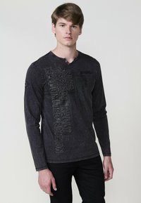 Fekete hosszúujjú póló V-kivágással, texturált mintával és fémes részletekkel az elülső részen, pamut denimből készült.