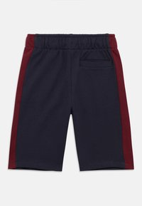 Σορτς σε ναυτικό μπλε με μπορντό ρίγα στο πλάι, διαθέτει ελαστική μέση και πίσω τσέπη. Κατασκευασμένο από μαλακό, αεριζόμενο ύφασμα.
