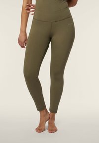 Leggings verde oliva con una vita alta, realizzati in un tessuto elastico. Presentano una texture liscia e un piccolo logo vicino all'anco.