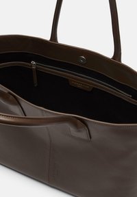 Brązowa skórzana torba na ramię z dwoma uchwytami, wyposażona w zapinaną na suwak wewnętrzną kieszeń oraz gładką fakturę. Delikatne tłoczone logo jest widoczne.