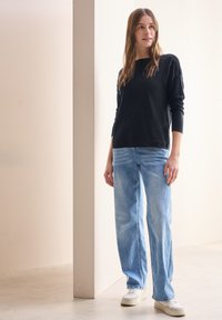 Svart långärmad topp, ljusblå vida jeans och vita sneakers. Släta texturer och avslappnad passform, mot en neutral bakgrund.