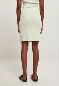 Falda de punto de canalé verde claro con un diseño ajustado, hasta la rodilla, que presenta aberturas laterales y un acabado suave. Llevada con sandalias planas negras.