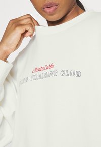 Felpa verde chiaro con una consistenza morbida, che presenta la scritta "Monte Carlo" in rosso e "BORG TRAINING CLUB" in blu sul petto.
