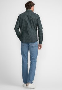 Groene gestreepte overhemd met lange mouwen en kraag, gecombineerd met lichtblauwe jeans en witte sneakers, gezien vanuit de achterkant.