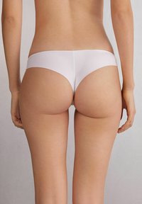 Witte naadloze stringonderbroek met een gladde textuur en minimale bedekking, voorzien van een low-rise ontwerp en strakke lijnen.