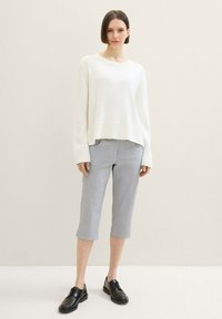 Weißer, gestrickter Pullover mit lockerer Passform, kombiniert mit grauen, cropped Hosen mit karierter Musterung, ergänzt durch schwarze Schnürschuhe.