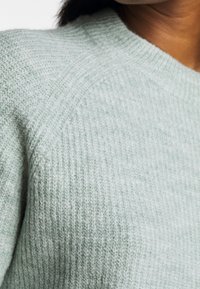 Ljusgrön stickad tröja med ribbad struktur och rund halsringning. Har en slät yta med subtila färgvariationer.