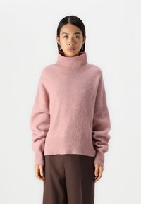 Hellrosa Pullover mit hohem Stehkragen, lockerer Passform und abgesenkten Schultern. Weiche, flauschige Textur mit gerippten Bündchen und Saum.