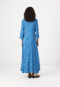 Langes, blaues Blumenkleid mit Dreiviertelärmeln, hergestellt aus leichtem Stoff. Verfügt über eine taillierte Taille und einen schwingenden Rock, der unterhalb der Knöchel endet.