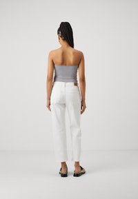 Jeans blancos con un corte relajado, combinados con una camiseta ajustada gris. Los jeans tienen bolsillos traseros y un parche de cuero marrón en la cintura.
