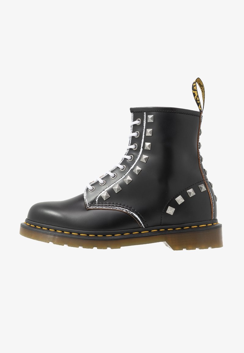 Botte en cuir noire à lacets avec clous carrés argentés, couture jaune sur la semelle et semelle en caoutchouc translucide marron.
