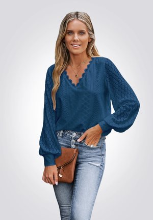 Marineblauwe blouse van textuur, met een patroon en pofmouwen, gecombineerd met lichtblauwe jeans en een bruin clutch.