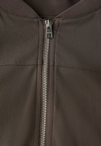 Brun zip-up jacka med en metallisk dragkedja, ribbad krage och slät textur med synliga sömdetaljer.