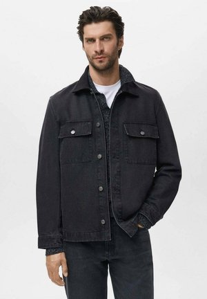 Zwarte denimjas met twee voorzakken, knoopsluiting en een kraag. Draag je over een donkergroene gebreide trui, gecombineerd met bijpassende zwarte jeans.