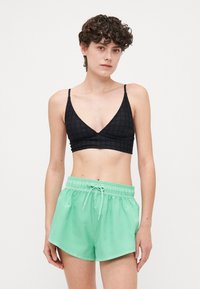 Fekete textúrájú bralette vékony pántokkal, mentazöld, zsinórral összehúzható rövidnadrággal párosítva. A rövidnadrág laza szabású és sima felületű.