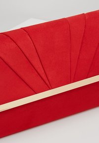 Pochette en daim rouge avec un design plissé en forme d’éventail sur le dessus et un accent métallique doré horizontal au centre.