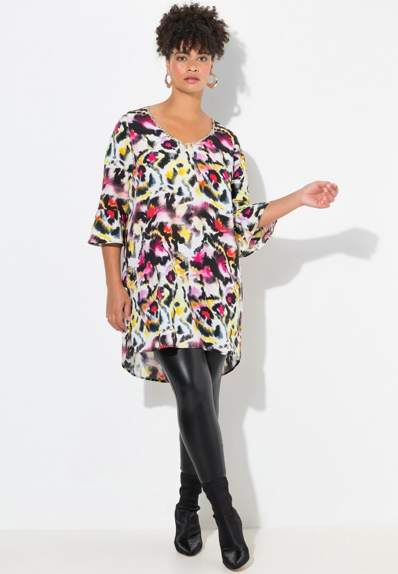 Mehrfarbige Tunika mit Leopardenmuster, mit Rundhalsausschnitt und drei Viertel-Glöckchenärmeln, kombiniert mit schwarzen Leggings und Stiefeletten.