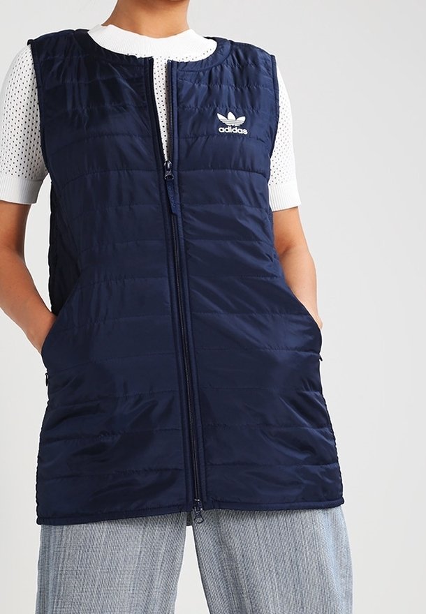 Marinblå vadderad väst med dragkedja fram och två sidofickor. Har Adidas-logotypen på bröstet. Slät textur och kviltad design.