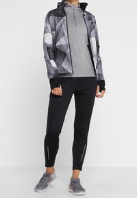 Completo sportivo composto da una giacca zip geometrica nera e grigia, una maglietta grigia a maniche lunghe, pantaloni neri aderenti e sneaker grigie con dettagli rosa.