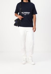 Granatowa bawełniana koszulka z białym nadrukiem logo, połączona z białymi spodniami o prostym kroju i białymi trampkami. Torebka z czarnego materiału z akcentami z metalu.