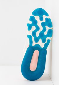 Podošvéd má modrý gumový povrch s vlnitým designem, kontrastní bílou mezipodešví a růžovým akcentem. Hladké textury po celém povrchu.