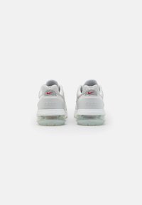 Vita sportskor i vitt med ovandel i mesh, gummisula och synlig luftdämpning. Har röda detaljer på hälen och varumärket.