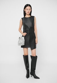 Fekete bőr ujjatlan ruha, testhez simuló sziluettel, térdig érő fekete csizmával és fényes ezüst táskával párosítva.
