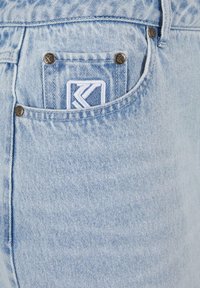 Jean en denim bleu clair avec une poche pour monnaie dotée de quincaillerie en métal et d'un logo brodé sur la poche. Texture douce et couture typique.