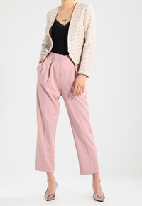 Světlobéžový vzorovaný blazer přes černý top na ramínka, v kombinaci s růžovými kalhotami s vysokým pasem a kovovými stříbrnými podpatky. Hladké textury a čisté linie.