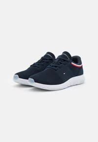 Laivastonsiniset verkkojuoksukengät valkoisella kumipohjalla. Ominaisuuksiin kuuluvat nauhat, pieni logotieto ja punavalkoinen raidallinen yksityiskohta sivulla.