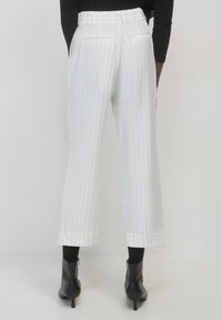 Pantaloni bianchi a gamba larga con righe verticali, vita elastica, tasche laterali e polsini. Indossati con stivaletti neri alla caviglia.