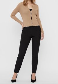 Cardigan rigato marrone chiaro con orlo a scallop e bottoni, abbinato a pantaloni neri slim e tacchi alti neri.