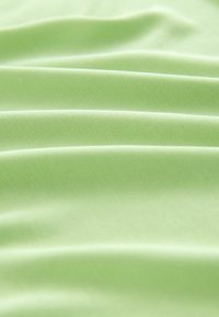 Tissu vert clair à la texture lisse, présentant des plis doux et un léger éclat, indiquant un matériau léger, possiblement en polyester ou en coton.