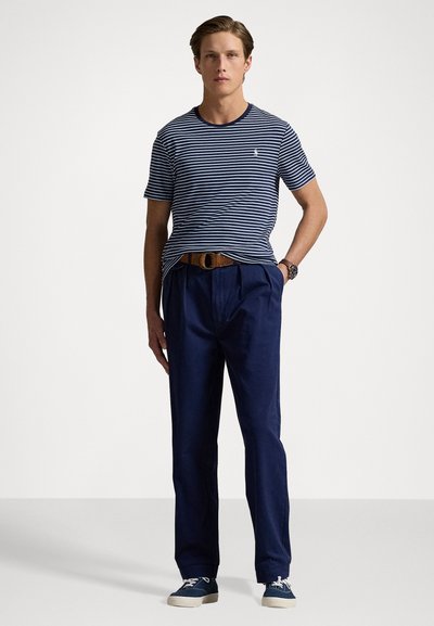 Tamsiai mėlyni ir balti dryžuoti trumpomis rankovėmis marškiniai, derinami su tamsiai mėlynomis kelnėmis, ruduo diržu, mėlynais sportbačiais ir subtiliu logotipu ant marškinio.