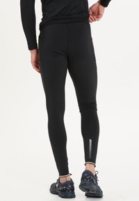 Zwarte sportleggingen gemaakt van rekbare stof, met een aansluitend ontwerp, reflecterende accenten nabij de enkel en piping naden.