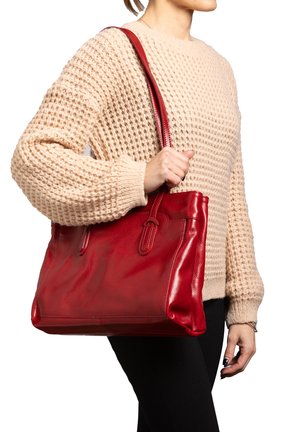 Borsa a spalla rossa in pelle con una texture liscia, doppi manici e dettagli sottili sui lati. Modello che indossa un maglione beige a maglia e pantaloni neri.