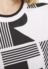 Black and white sweater featuring bold geometric patterns, including stripes and shapes, with a round black ribbed neckline.