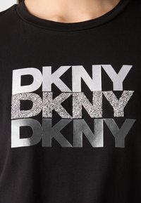 T-shirt in cotone nero con logo sovrapposto "DKNY" in argento metallico e dettagli glitterati in argento, con un classico scollo rotondo.