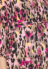 Vestido com padrão floral em rosa, preto e amarelo, apresentando um laço na cintura e mangas curtas dobradas. Tecido suave e texturizado.