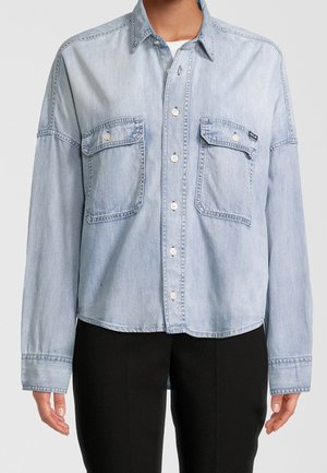 Lichtblauw denim overhemd met lange mouwen, twee borstzakken, knopen aan de voorkant en een afgeronde zoom. Heeft een ontspannen pasvorm en zichtbare stikdetails.