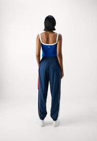 Blå stripete crop-top med hvite stropper og en logo på baksiden, kombinert med marineblå joggebukser som har røde og hvite sideakenter og elastiske mansjetter.