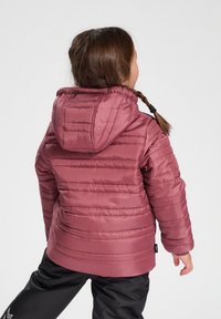 Doudoune rose avec capuche, présentant un design matelassé horizontal, des poignets élastiques et une texture lisse. Associée à un pantalon noir.