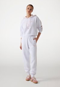 Witte cropped hoodie met roze logo, gecombineerd met witte joggingbroek met zijstrepen en roze sneakers met een gestructureerde zool.