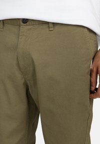 Khakihosen aus einem glatten, strukturierten Stoff. Mit Knopfverschluss und Seitentaschen. Der Bund ist zur Haltbarkeit genäht.