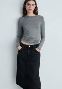Grå langærmet top kombineret med en sort denim maxiskørt med forlommer og knaplukning, der præsenterer et afslappet lag-på-lag look.