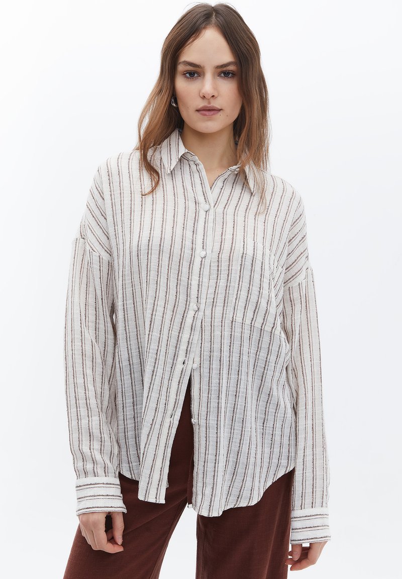 Camicia a maniche lunghe in tessuto leggero, con strisce verticali beige e marroni, abbottonatura frontale e una vestibilità rilassata con polsini arrotolati.