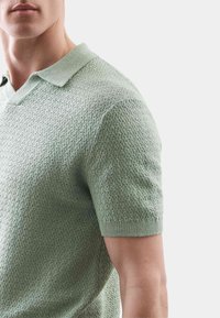 Polo s krátkým rukávem ve světle zelené barvě, se strukturovaným pleteným vzorem, límečkem a přiléhavým střihem.
