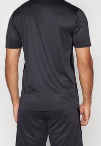 Czarna sportowa koszulka z krótkim rękawem o fakturowanej tkaninie i akcentach na bocznych panelach, odpowiednia do uprawiania sportu lub aktywnego trybu życia.