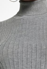Gros plan sur un pull à col roulé côtelé gris porté par une personne, montrant la texture et les motifs de tricot verticaux.